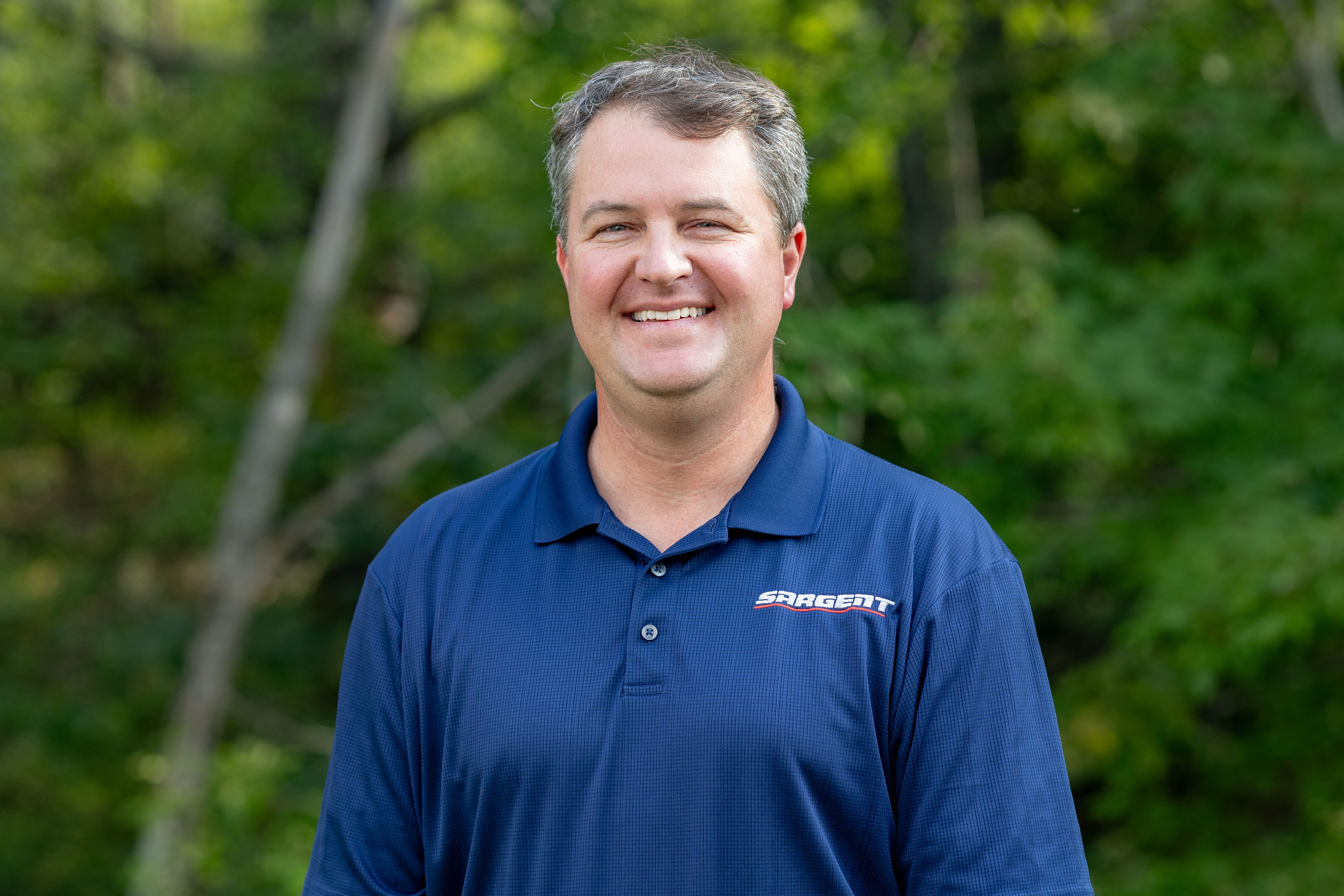 a man smiling in front of a forest for a picture
